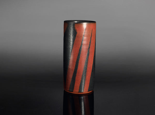 Cylindrical vase with black and red striped design on a gray background