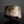 Load image into Gallery viewer, A handmade ceramic sake cup with a textured, organic glaze featuring mottled shades of brown, gray, pink, and gold, set against a dark reflective background.
