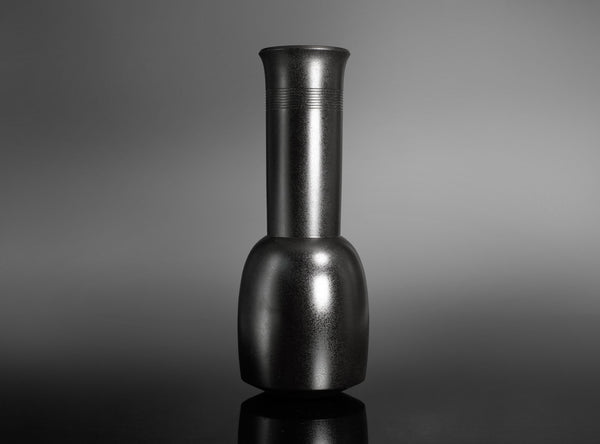 A Bronze Kinuta Flower Vase with a flared cylindrical neck and a rounded base, standing on a reflective black surface against a gray gradient background.