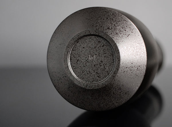 A close-up of a Bronze Kinuta Flower Vase, photographed on a reflective dark surface against a gray studio background.