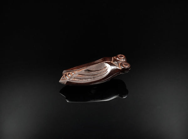 A finely cast bronze kōgō in the form of a cicada, shown on a glossy black reflective surface against a black background.