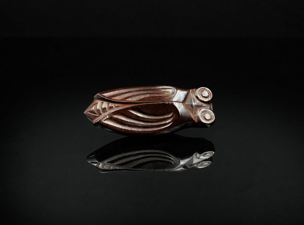 A finely cast bronze kōgō in the form of a cicada, shown on a glossy black reflective surface against a black background.