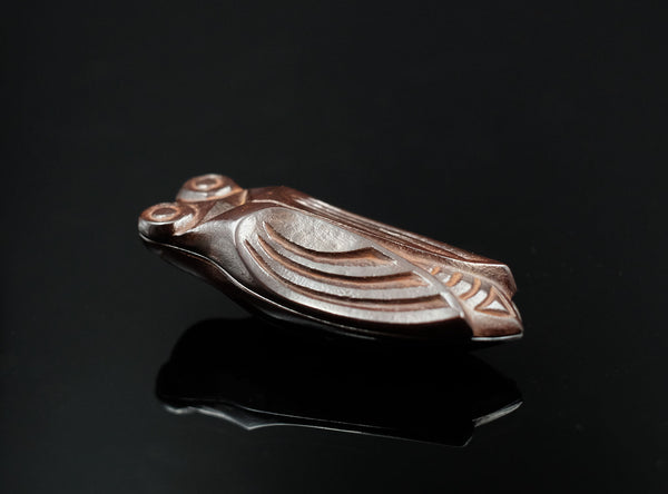 A finely cast bronze kōgō in the form of a cicada, shown on a glossy black reflective surface against a black background.