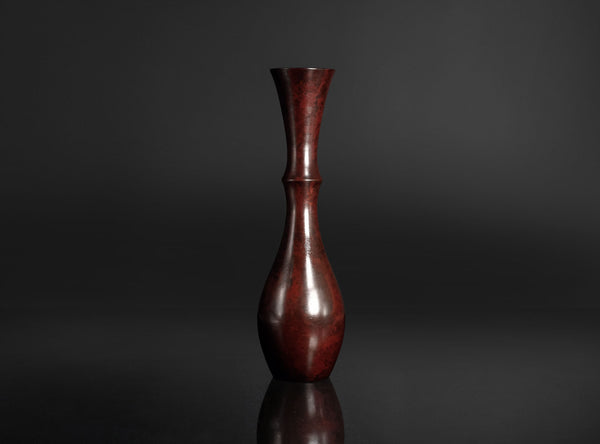 A dark reddish-brown wooden vase with a flared neck and bulbous body, standing on a reflective black surface against a dark gray background.