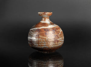 A small handmade ceramic vase with a bulbous body and short neck, featuring a marbled glaze in earthy brown, beige, and white tones, set against a dark reflective background.
