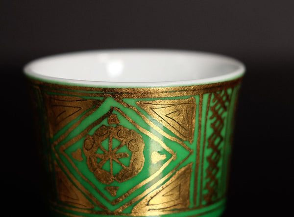 Decorative cup with green and gold patterns on a dark background