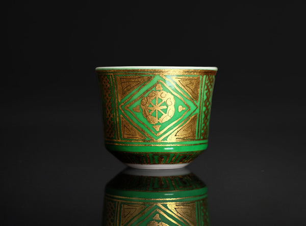 Green ceramic cup with gold geometric patterns on a black background