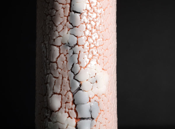 A close-up of a cylindrical product with a textured, cracked surface showing white and light gray sections over a warm peach-pink base, set against a solid black background.
