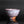 Load image into Gallery viewer, A handmade ceramic tea bowl with a textured, speckled glaze in earthy brown, white, and muted pink tones, shown on a reflective black surface against a dark gray background.
