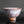 Load image into Gallery viewer, A handmade ceramic tea bowl with a textured, speckled glaze in earthy brown, white, and muted pink tones, shown on a reflective black surface against a dark gray background.
