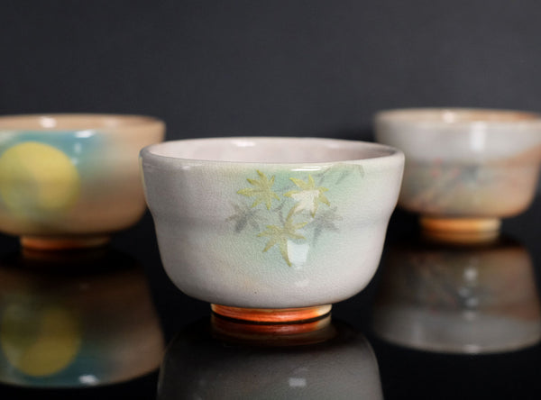 Three ceramic cups with floral patterns on a reflective surface and dark background