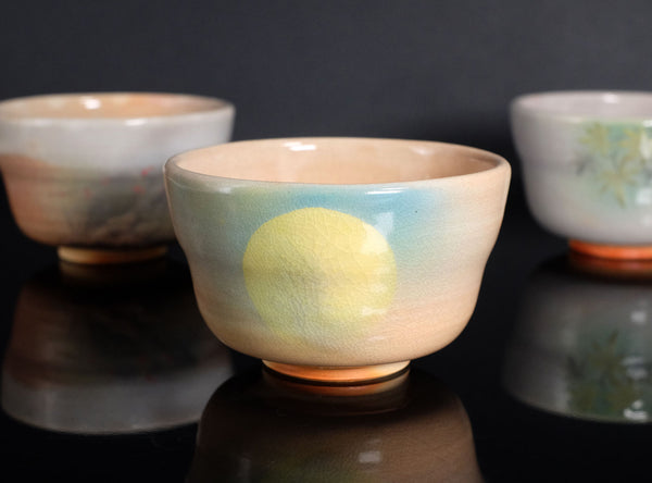 Three ceramic cups with different designs on a reflective surface