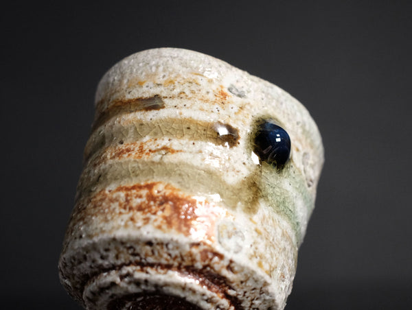 Close-up of a ceramic cup with textured surface and dark eye on a black background