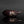 Load image into Gallery viewer, A sculptural eggplant-shaped object with a glossy dark purple body and textured brown stem, photographed on a reflective black surface against a dark gray background.
