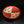 Load image into Gallery viewer, A ceramic bowl with a split design, featuring a red outer rim, one half with red diagonal stripes on an off-white background, and the other half with terracotta-colored segments. The bottom half also has small red and green fish-like motifs on an off-white background, set against a dark reflective background.
