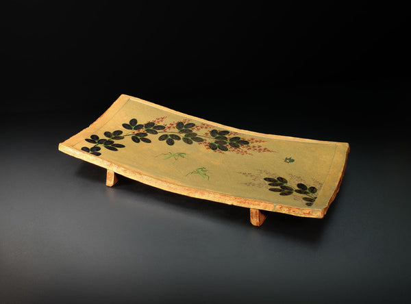 A rectangular ceramic serving tray with a light beige painted surface, decorated with black leaf motifs and small red berry accents, shown on a dark studio background.