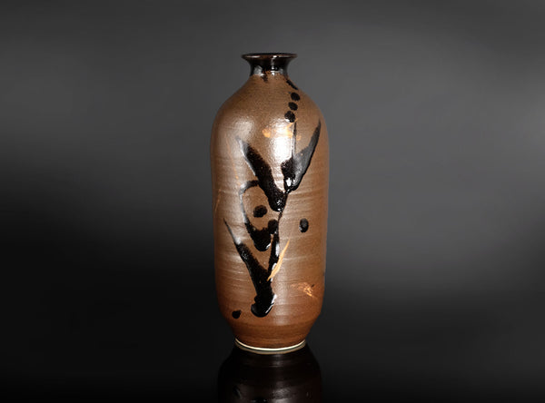 A brown ceramic vase with a glossy finish, featuring a black brushstroke floral pattern and small black dots, set against a dark gray gradient background.
