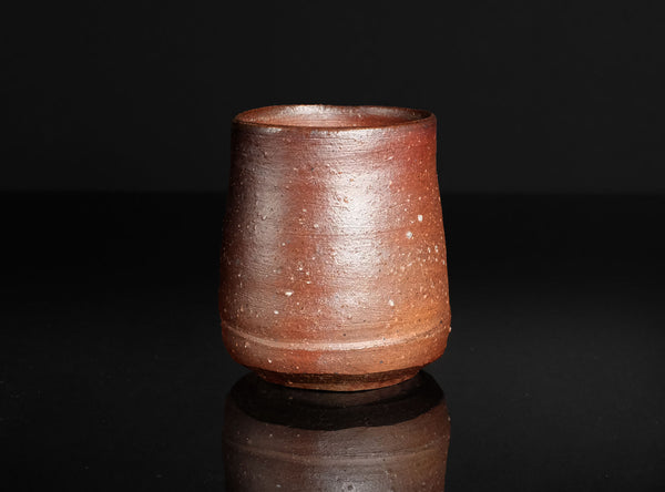 Brown ceramic cup on a reflective black surface with a dark background