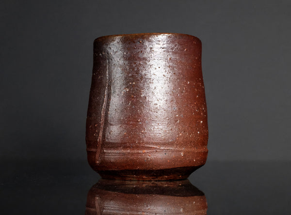 Brown ceramic cup on a reflective surface with a dark background