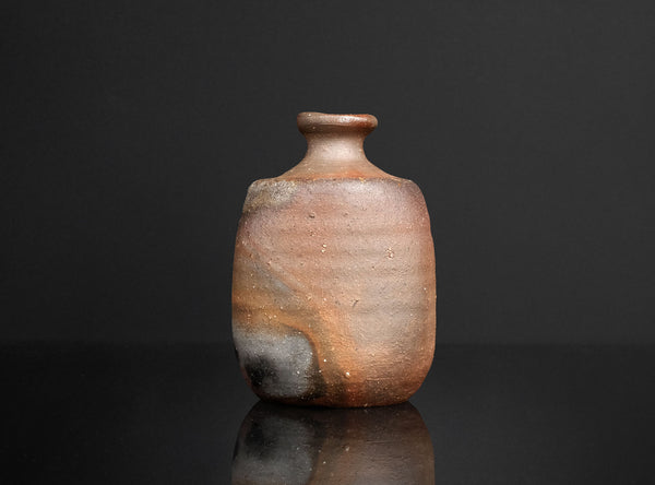 Small ceramic bottle with a textured surface on a reflective black surface and dark background