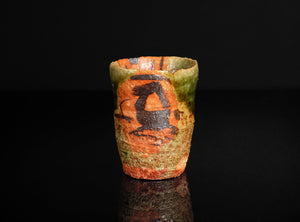 Small ceramic cup with decorative design on a black background