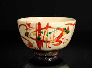 Decorative ceramic bowl with red and green abstract designs on a black background