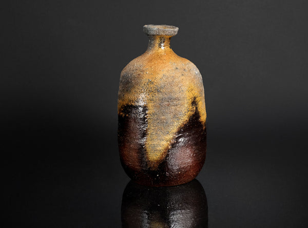Rustic ceramic sake with a dark brown and yellow glaze on a black background