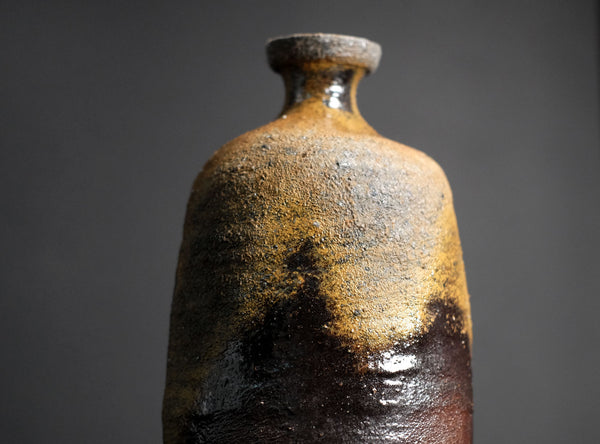 Brown ceramic sake bottle with textured surface on a gray background