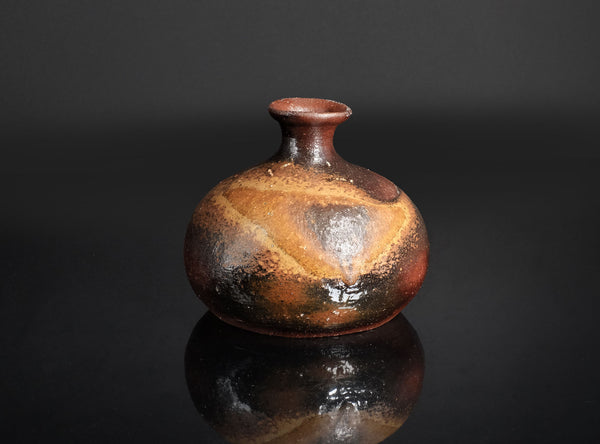 Small ceramic jar with brown and black glaze on a reflective black surface