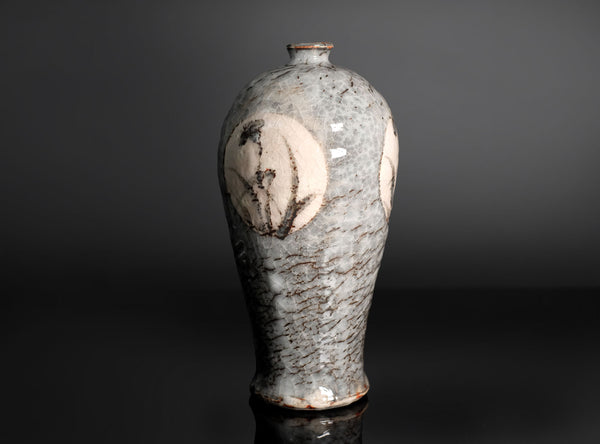 A ceramic vase with a pear-shaped body, featuring a textured gray and white glaze with brown speckles and hand-painted floral motifs on the sides, set against a dark gray background.