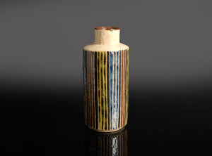Cylindrical ceramic sake bottle with striped design on a dark background