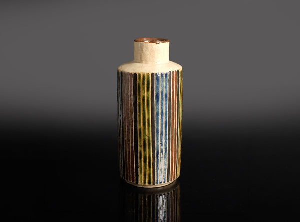 Cylindrical ceramic sake bottle with striped design on a dark background