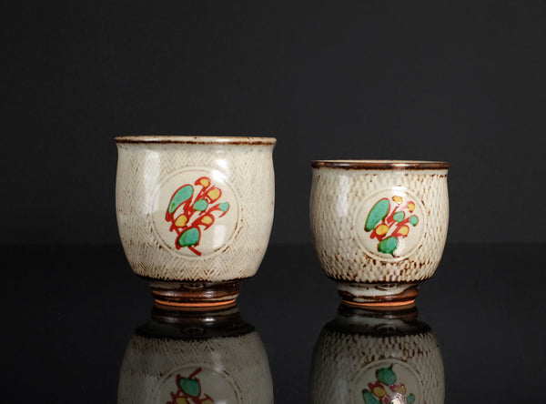 Two ceramic cups with decorative designs on a reflective surface.