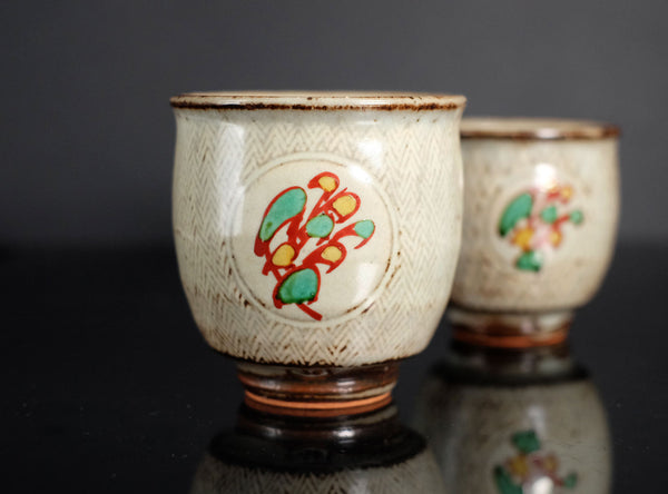 Two ceramic cups with decorative designs on a reflective surface.