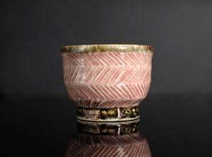 A rounded copper-red tea cup from Tatsuzo Shimaoka’s Mashiko practice, enlivened by pale cord patterns across a softly coloured pink ground. Its lower, broader proportions give it a generous open profile, offering a distinct counterpart to the taller cup with which it was originally paired.

The body curves inward beneath the wide mouth, then rounds towards a short, clearly defined circular foot. A lightly flaring rim frames the pale glazed interior. The changing contours give the cup a comfortable visual b