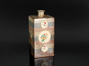 A distinctive square jar by Tatsuzo Shimaoka, combining a firm architectural form with bands of inlaid decoration and colourful floral roundels. Its cream, muted blue and pinkish-brown palette brings warmth to the straight-sided body, while the patterned surfaces reflect the artist’s inventive approach to Mashiko pottery.

The tall rectangular body rises to a broad, nearly flat shoulder and a short cylindrical neck. A gently flaring lip softens the transition between the angular vessel and its circular open