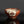 將圖片載入到圖庫檢視器中， A handmade ceramic tea bowl with a glossy reddish-brown glaze, featuring a hand-painted floral motif in red, green, and black on a white patch on the front, set against a dark gray background with a reflective surface below.
