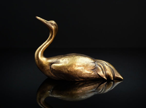 Bronze swan sculpture on a reflective surface with a black background