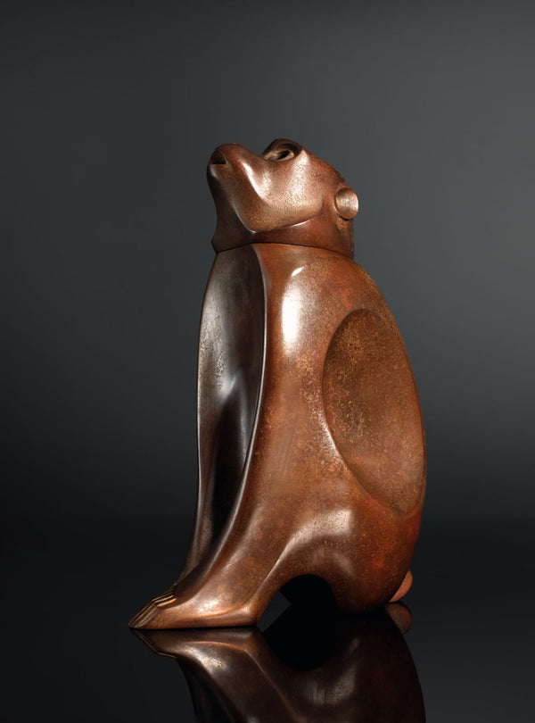 A sculptural monkey-shaped incense burner by Tsuda Eiju, distinguished by its upright seated pose and smoothly modelled brown surface. The animal raises its face, creating a lively expression while retaining the compact, self-contained outline of a small metal sculpture.

The rounded body rests on its haunches, with long forelimbs descending towards the base. A broad oval area defines the flank, introducing a shallow change in contour against the curved torso. The head is carefully simplified, with projecti