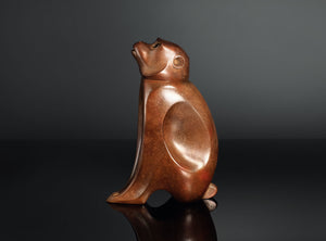 A sculptural monkey-shaped incense burner by Tsuda Eiju, distinguished by its upright seated pose and smoothly modelled brown surface. The animal raises its face, creating a lively expression while retaining the compact, self-contained outline of a small metal sculpture.

The rounded body rests on its haunches, with long forelimbs descending towards the base. A broad oval area defines the flank, introducing a shallow change in contour against the curved torso. The head is carefully simplified, with projecti
