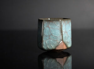 Ceramic sake cup with a textured surface on a reflective black surface