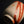 Load image into Gallery viewer, A close-up of a handmade ceramic tea cup with a textured beige clay body and diagonal reddish-brown glaze stripes, set against a dark gray background with a reflective black surface below.
