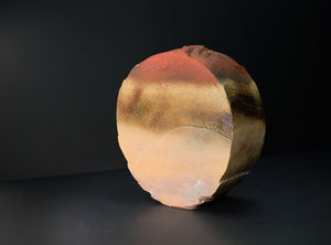 A spherical decorative stone sculpture with a textured, polished surface showing natural earthy color variations of terracotta, ochre, and brown, set against a dark studio background.