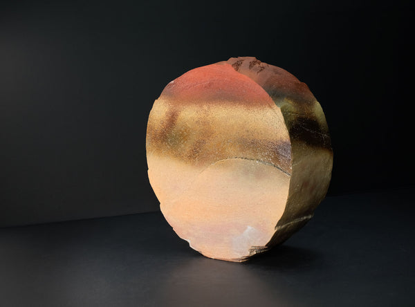 A spherical decorative stone sculpture with a textured, polished surface showing natural earthy color variations of terracotta, ochre, and brown, set against a dark studio background.