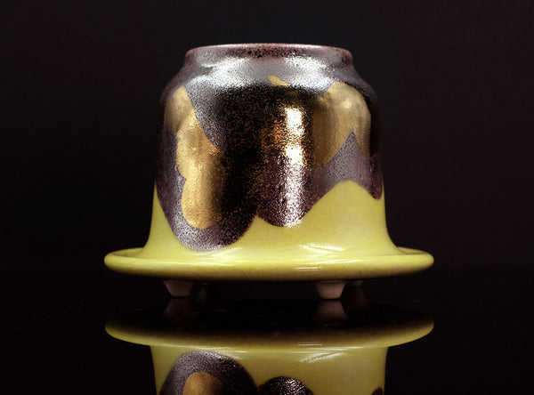 Ceramic container with gold and black glaze on a reflective surface