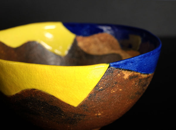 Wooden bowl with yellow and blue geometric design on a dark background