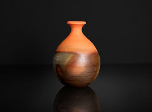 Two-toned ceramic vase on a black reflective surface with a dark background