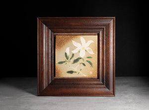 Framed artwork of a white flower with green leaves on a gold background