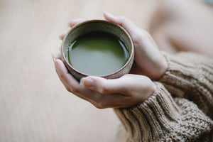 Woman has a cup of green tea in hand.